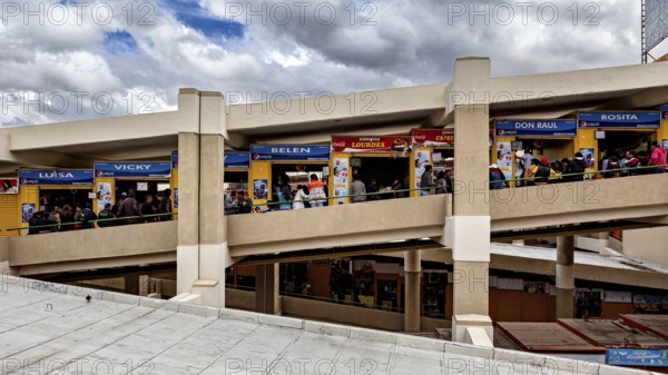 Long view of the upper floor of a market with colourful stalls and many customers, Small shops and