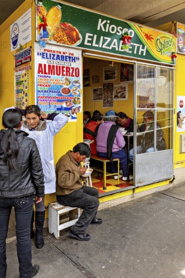 Small food stall with yellow walls, people sitting and eating, menu posters on the wall, Small