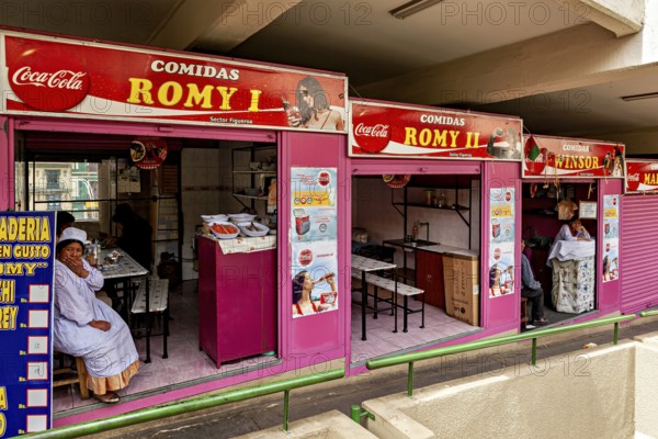Food stalls with pink awnings and colourful signs, people waiting in a market hall, Small shops and