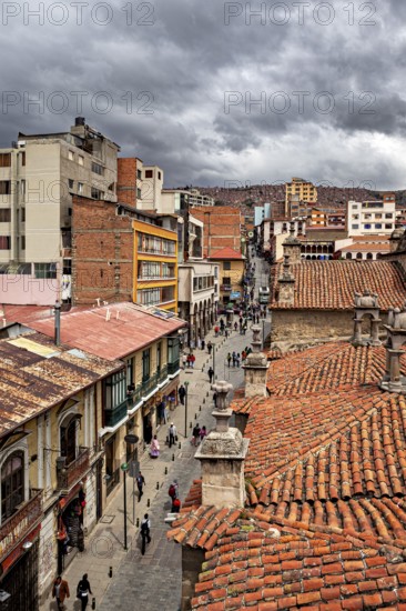 Historic city view with red tiled roofs under a cloudy sky, people in the streets of La Paz in