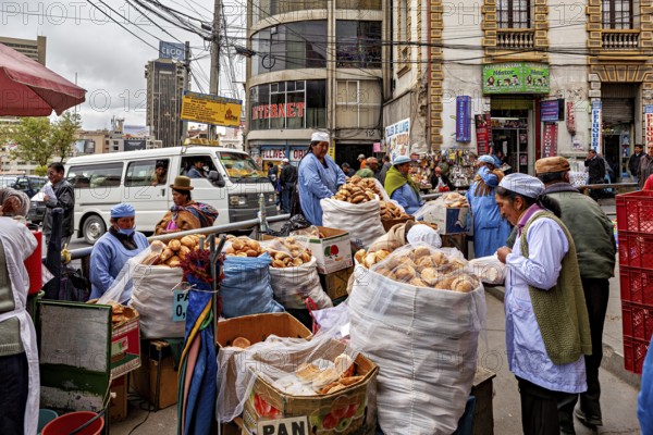 A bustling city market with bread stalls and vendors in a busy street between tall buildings, woman