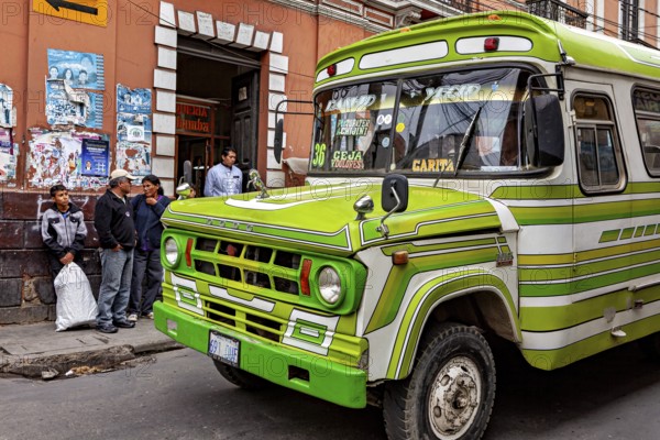 Green retro bus in front of a municipal building with people on the pavement, The colourful buses