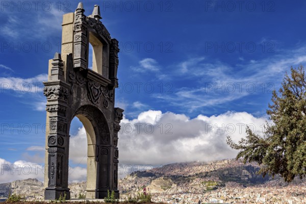 A stone gate with ornate decorations in front of a sprawling cityscape and a blue sky, The gate at