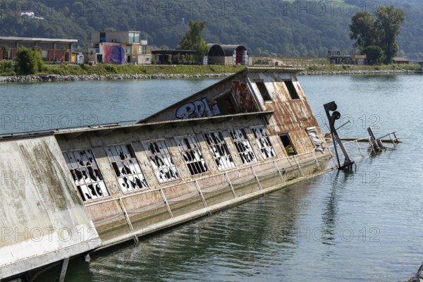 Partially submerged ship with graffiti near shore with mountains, at the harbour Linz Upper Austria