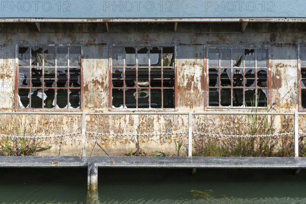 Abandoned building with broken windows and rust next to a body of water, at the harbour of Linz