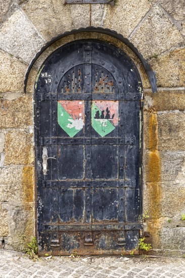 Old door with coat of arms on a stone wall, surrounded by rust and weathering, Pöstlingsbergkirche