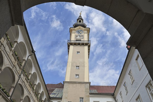 Historic clock tower above an inner courtyard with sky and surrounding arcades, Arkardenhof
