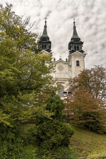 Historic church with two towers behind autumnal trees in front of a cloudy sky, Pöstlingsbergkirche