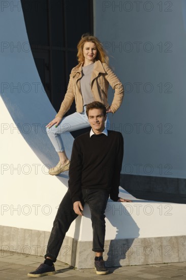 A young couple enjoys a sunny day in an urban area, posing creatively at a striking architectural