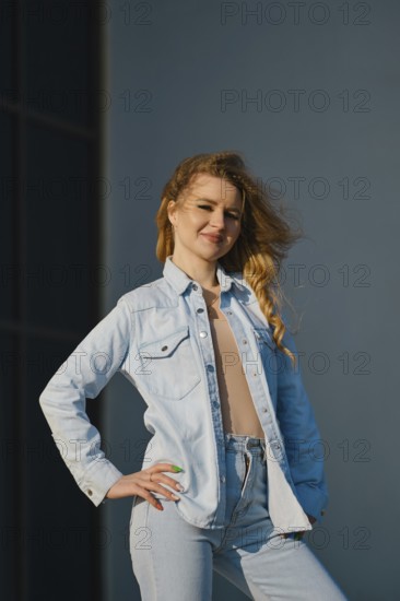 A young woman stands confidently, showcasing a light denim jacket and high-waisted jeans. The