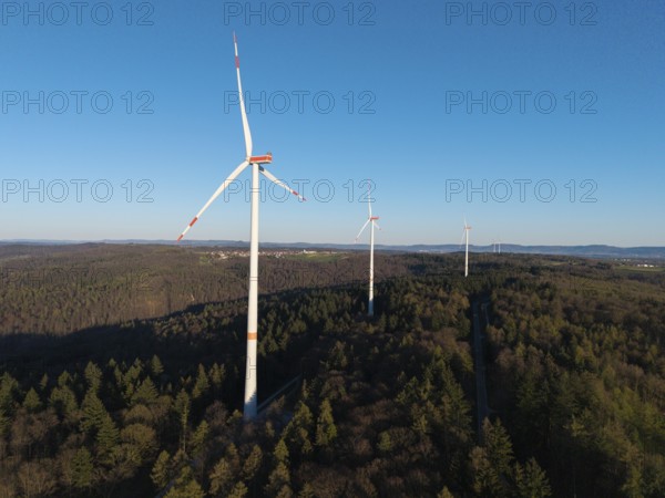 Wind turbines rise above the forest under a cloudless blue sky, near Schorndorf im Remstal,