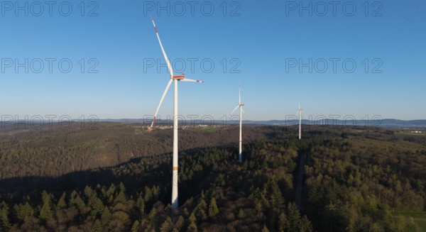 Several wind turbines tower above the treetops of a forest under a blue sky, near Schorndorf in the