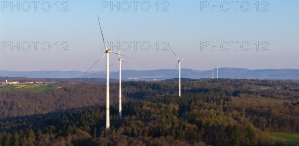 Wind turbines stand on a forest landscape with a clear blue sky in the background, near Schorndorf