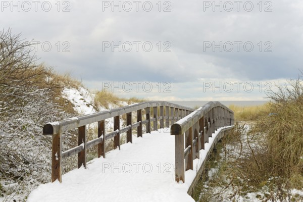 Winter day, onset of winter, wooden plank path leads through the snow-covered dune landscape to the