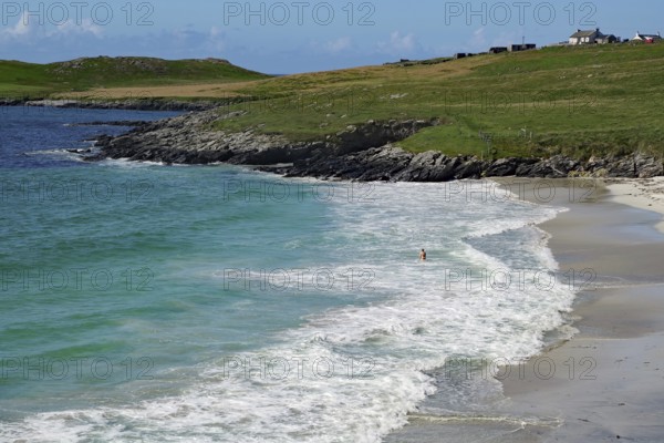 Coastline with white sand and gentle waves on a clear blue day, solitary figure in the water,