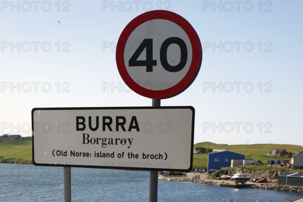 A road sign on an island with a clear blue sky and a body of water in the background, reference to