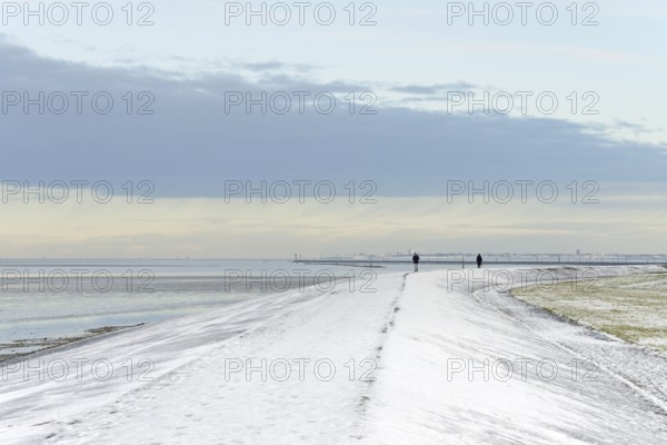 North Sea coast on a winter's day, people walking over a snow-covered dyke, the island of Norderney
