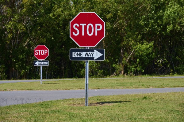 Stop signs and one-way street signs in front of a green tree landscape, Flamingo, Everglades