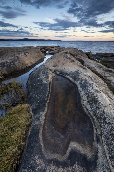 Rocky coastline with water puddles and grass during a sunset-lit evening, Skjeberg, Sarpsborg,