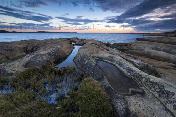 Large rocks with puddles on the coast during a sunset with clouds in the sky, Skjeberg, Sarpsborg,
