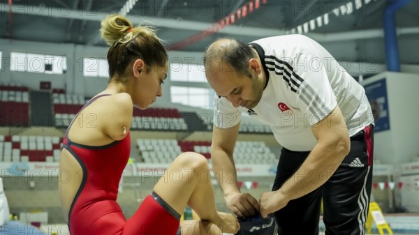 A coach assists a female swimmer with limb loss in adjusting her swim cap before training in an