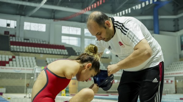 A coach assists a female swimmer with limb loss in adjusting her swim cap before training in an