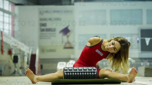 A female Paralympic swimmer with amputated arms performs warm-up exercises on a mat before entering
