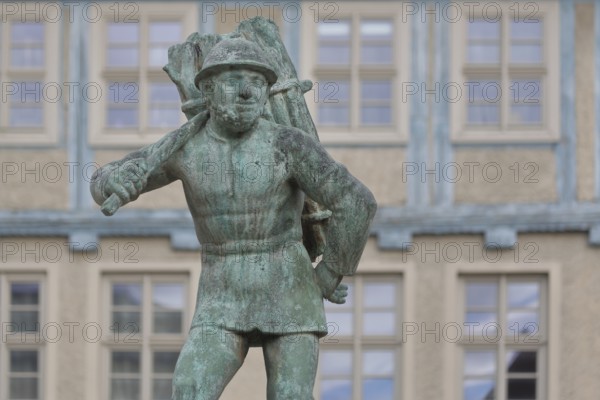 Wood carrier by Bernhard Frydag, 1914, male figure carrying basket with wood on his back, symbol