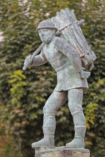 Wood carrier by Bernhard Frydag, 1914, male figure carrying basket with wood on his back, symbol