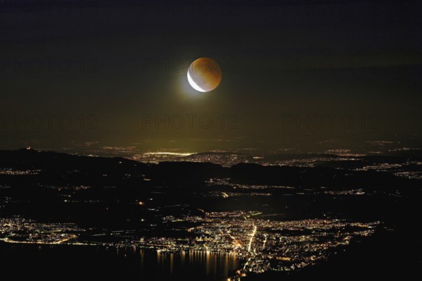 Blood moon, total lunar eclipse over the illuminated city and Lake Zug, Zug, Canton Zug,