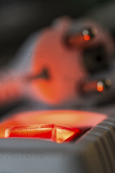 Close-up of a white power plug, Schuko plug, on a multiple socket with red indicator light,