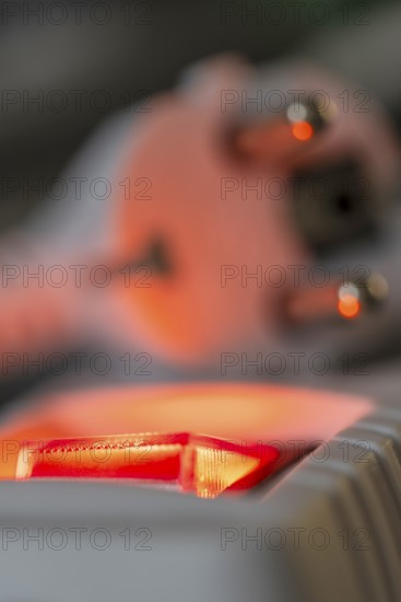 Close-up of a white power plug, Schuko plug, on a multiple socket with red indicator light,