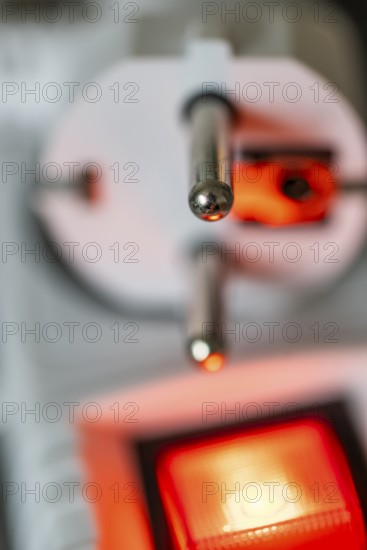 Close-up of a white power plug, Schuko plug, on a multiple socket with red indicator light,