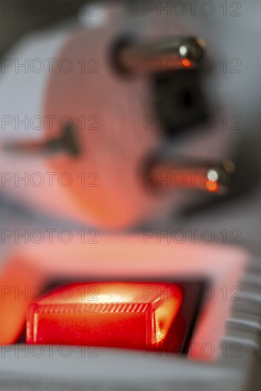 Close-up of a white power plug, Schuko plug, on a multiple socket with red indicator light,