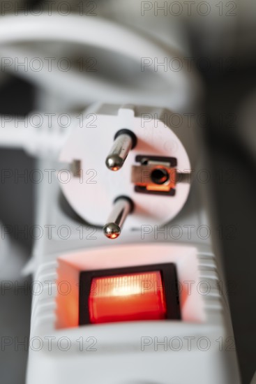 Close-up of a white power plug, Schuko plug, on a multiple socket with red indicator light,