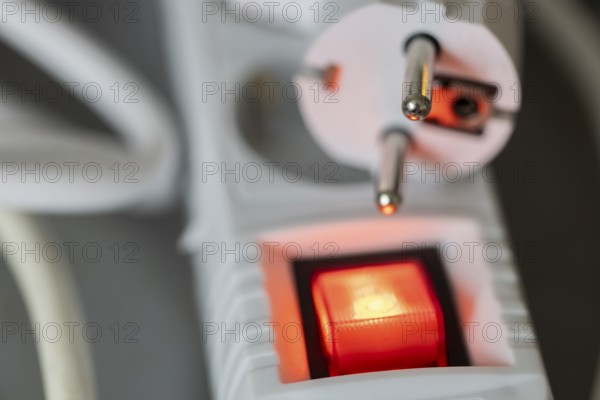 Close-up of a white power plug, Schuko plug, on a multiple socket with red indicator light,