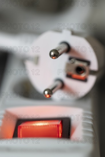 Close-up of a white power plug, Schuko plug, on a multiple socket with red indicator light,