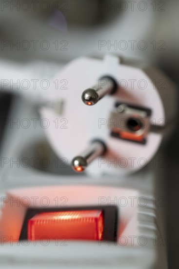 Close-up of a white power plug, Schuko plug, on a multiple socket with red indicator light,