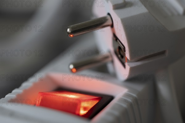 Close-up of a white power plug, Schuko plug, on a multiple socket with red indicator light,