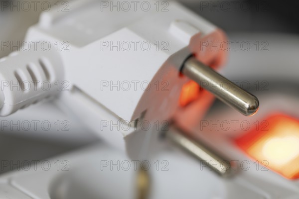 Close-up of a white power plug, Schuko plug, on a multiple socket with red indicator light,