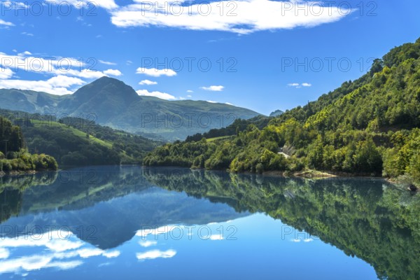 The serene ibiur reservoir in tolosa, gipuzkoa, reflects the surrounding mountains and blue sky
