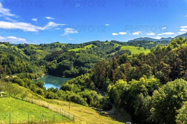 Ibiur reservoir reflects the vibrant blue sky amidst the rolling green hills and lush forests of