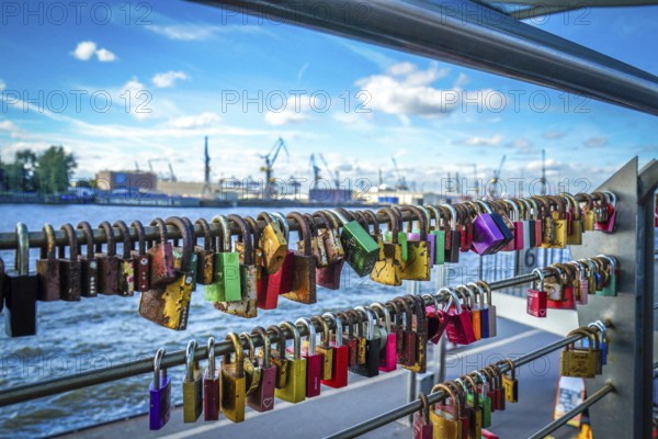 Many colourful love locks on a railing with a view of the harbour and cranes. View from the jetties