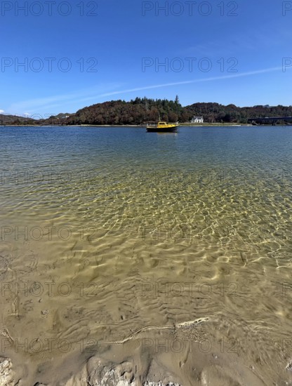 Clear water on a beach with a view of a yellow boat and wooded island in the background, Silver