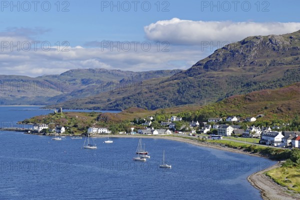 Coastal town with sailing boats at the harbour, mountains in the background, under blue sky, Kyle