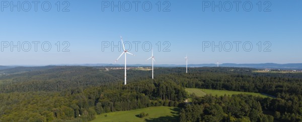 Wind turbines stand above a wooded hill under a clear blue sky, near Schorndorf, Rems Valley,