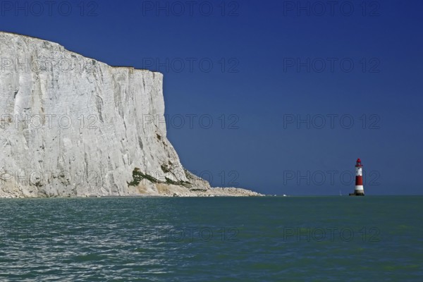 White cliff top next to a red and white lighthouse under a clear blue sky by the sea, Old Harrys