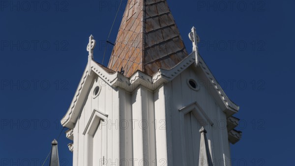 Pointed church tower with wooden elements and clear blue sky in the background, Tangen kirke or