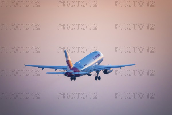 A Eurowings aeroplane takes off and disappears into an orange evening sky, Stuttgart,