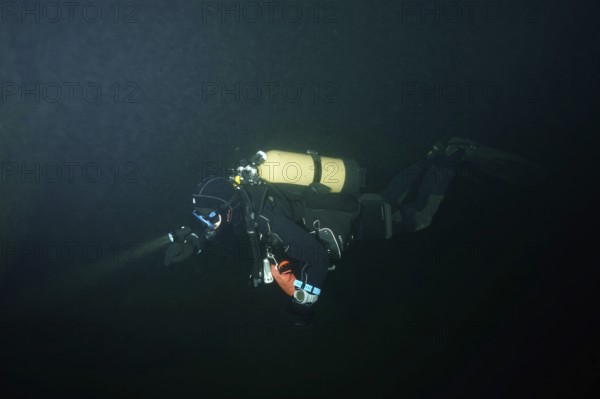 A diver in a diving suit explores a dark underwater environment. Dive site wreck of the Jura, Lake